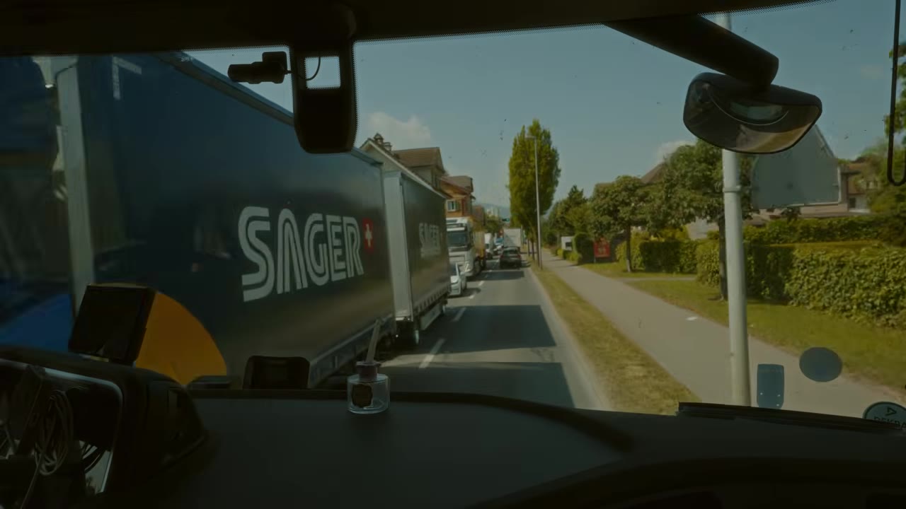 Впереди грузовик с логотипом «SAGER», по сторонам деревья и жилые дома