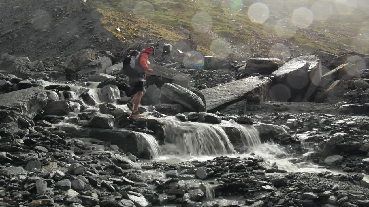 Турист в красной куртке у горного ручья среди каменной россыпи